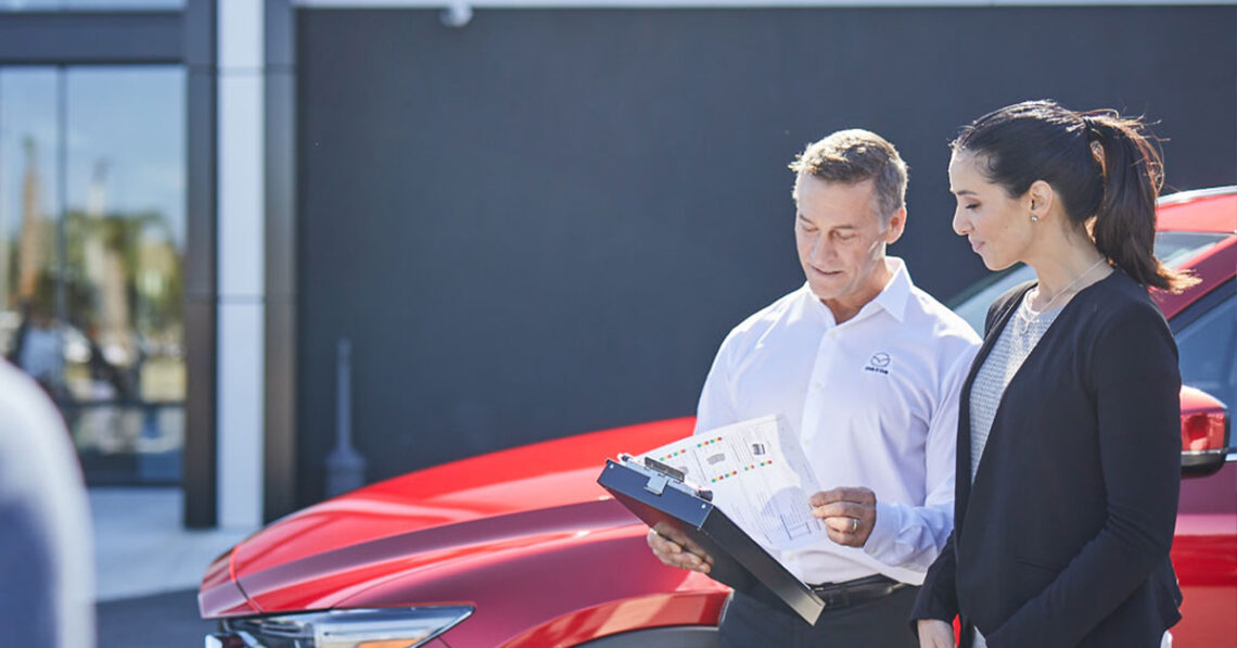 Female car owner and male service technician talking in front of Mazda car at service center